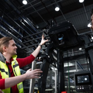 Linde Material Handling intralojistik danışmanı, otomatik araç bulunan depo ortamında bir müşteriyle görüşme gerçekleştiriyor.