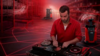 Bir DJ, depoda miksaj masasının başında dururken arka planda Linde Material Handling otomatik araçları yer alıyor.